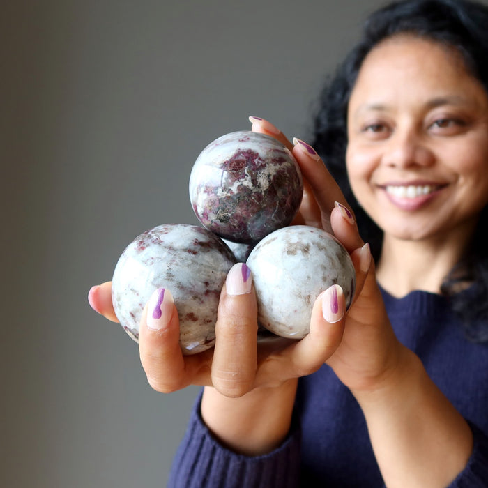 sheila of satin crystals holding up a pile of tourmaline quartz spheres