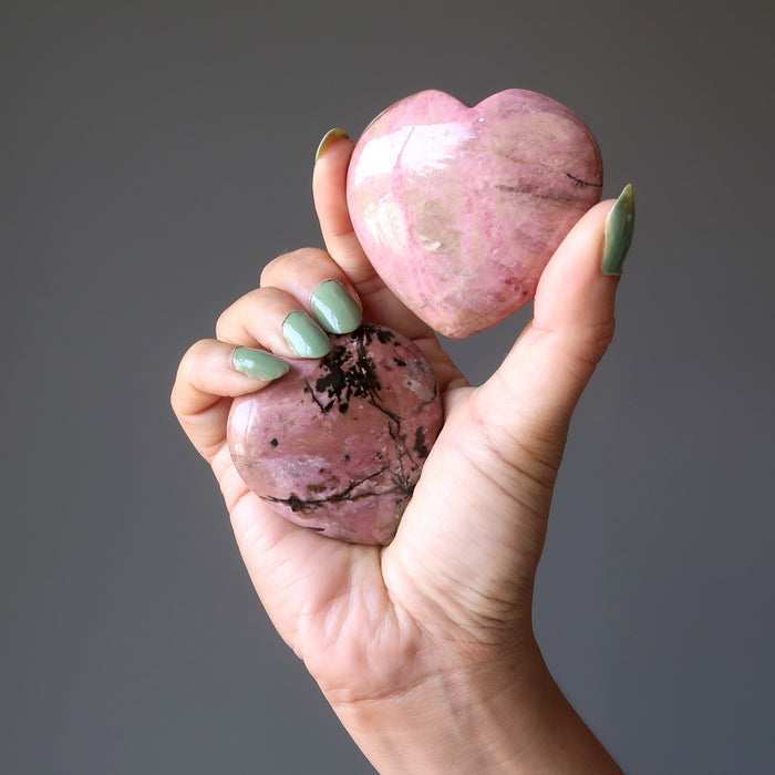 hand holding two pink and black rhodonite hearts