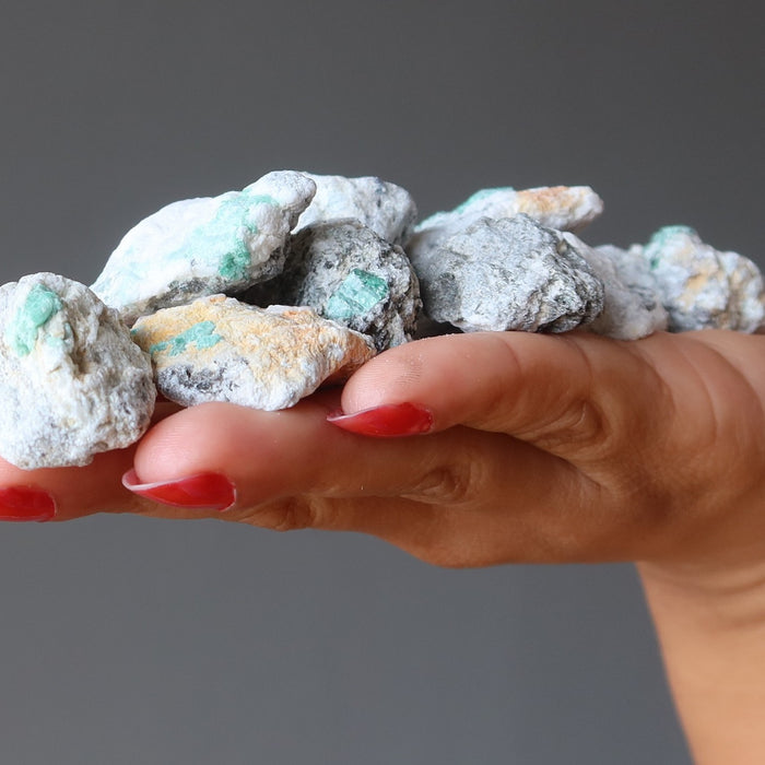 hand holding pile of raw emeralds