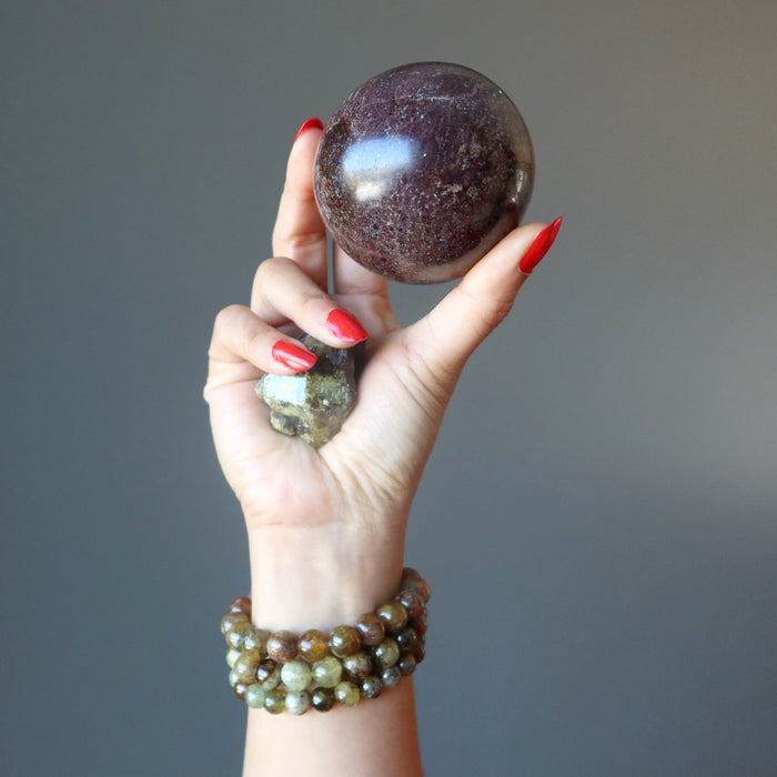 hand holding up garnet sphere, green garnet raw, wearing grossular garnet bracelets