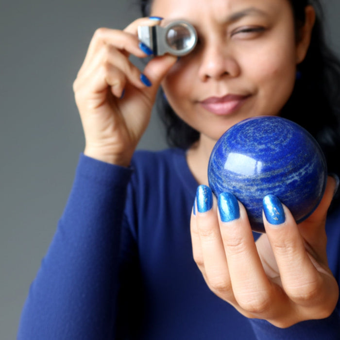 woman looking through diamond loupe at a lapis lazuli sphere