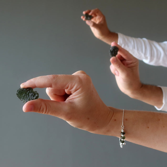 three hands holding raw moldavite