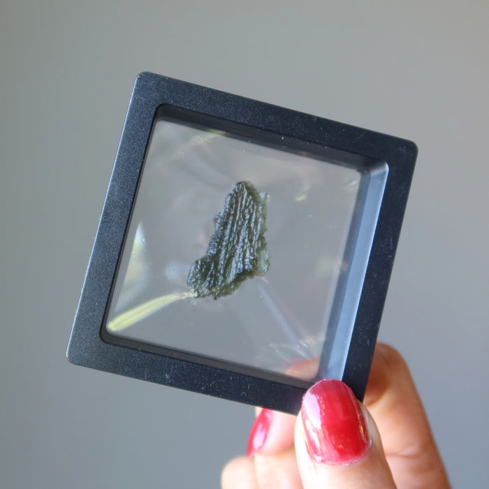 hand holding up a raw green moldavite in clear suspension display case