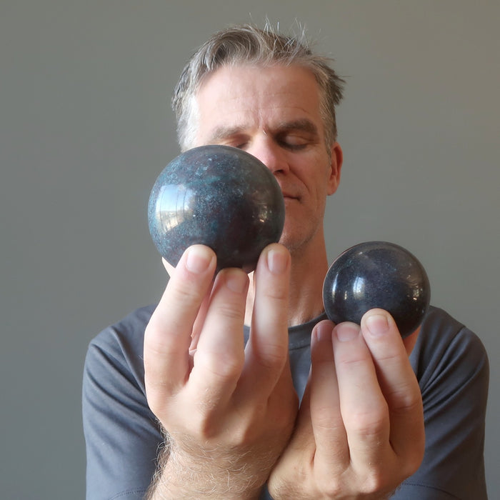 man with eyes closed holding two ruby kyanite spheres