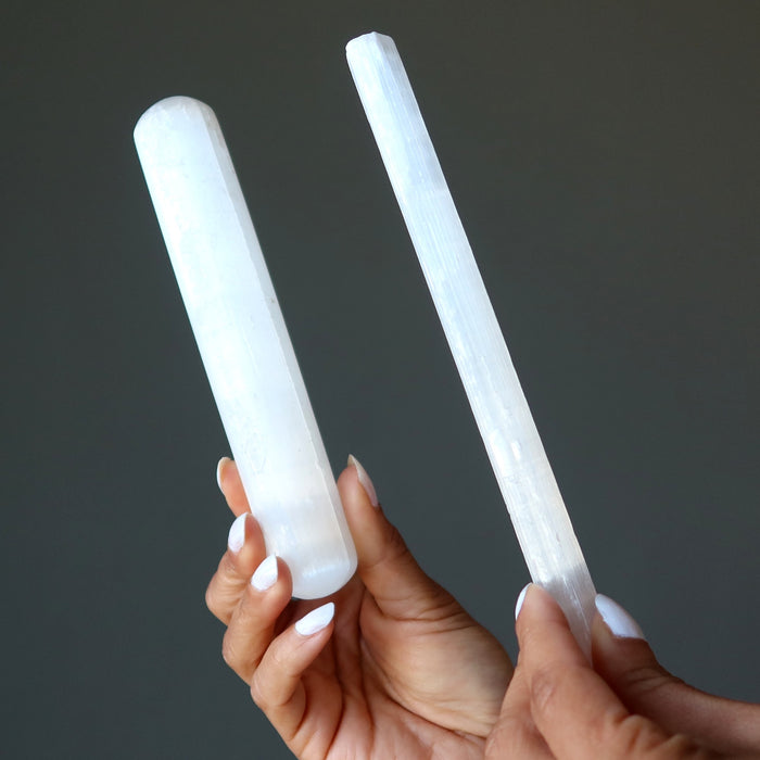 hands holding selenite massage wand and raw stick