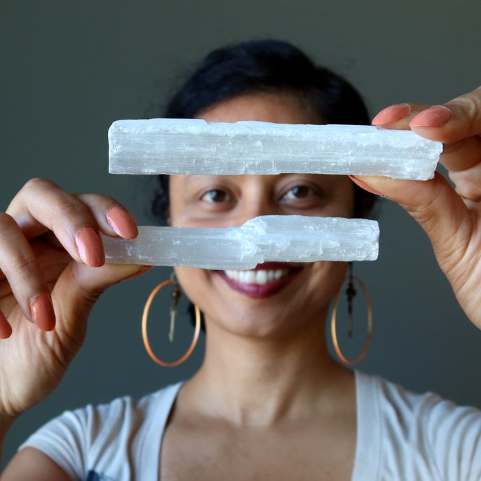 woman holding up two sticks of white selenite satin spar wands