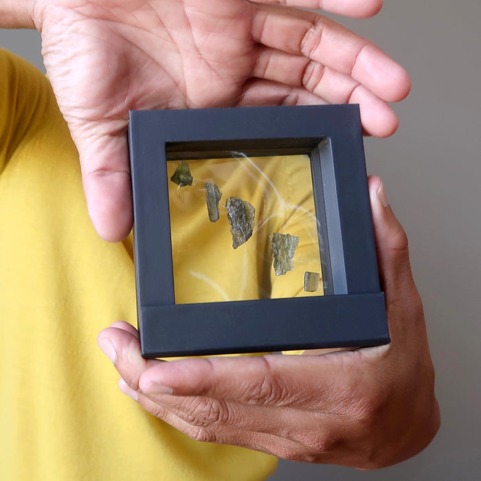 man holding 5 moldavite stones in a suspension frame