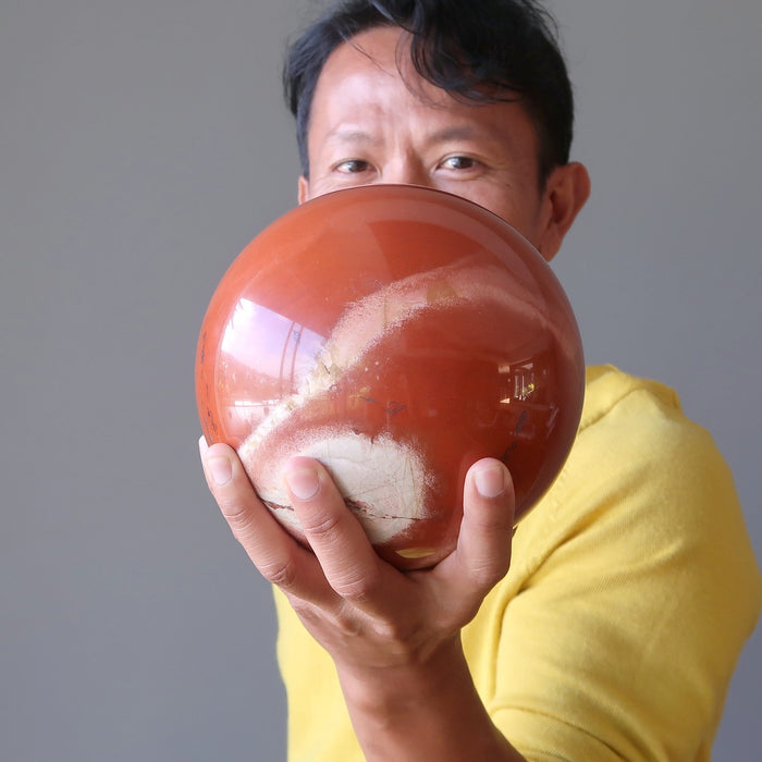 man holding a large red jasper sphere