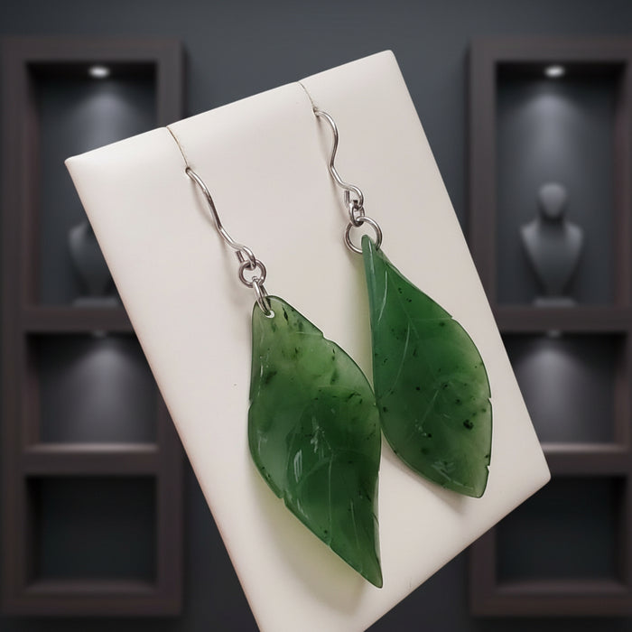 Green leaf-shaped earrings on a wooden surface