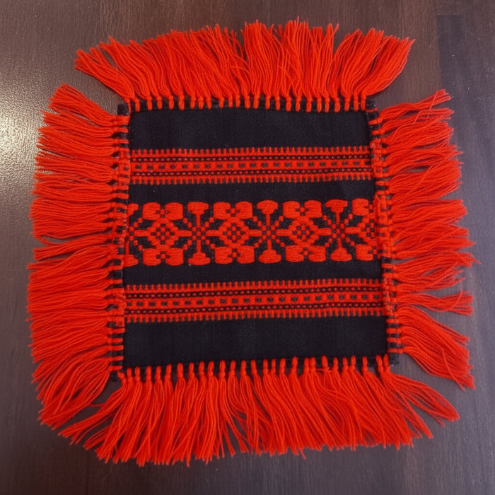 Square woven fabric with red pattern and fringes handmade in hungary on a dark background