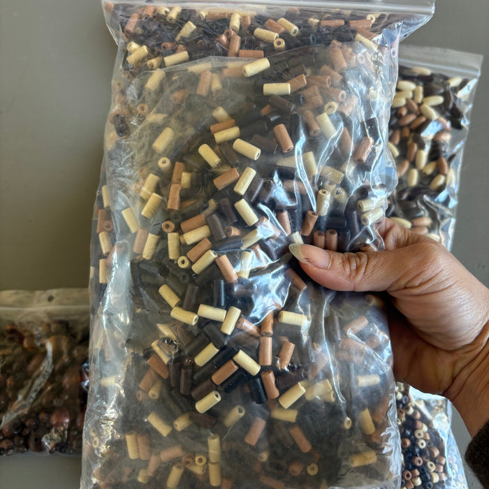 Hand holding a clear plastic bag filled with small wooden beads on a gray surface.