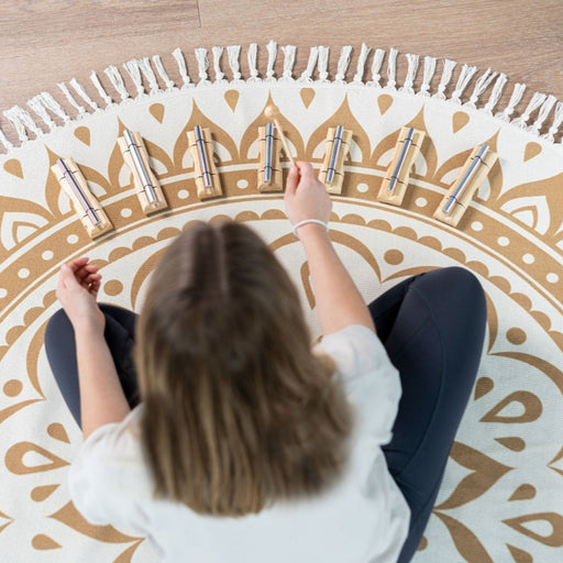 Person sitting on a decorative rug with heart patterns and playing a set of small instruments.