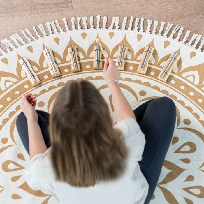 Person sitting on a decorative rug with heart patterns and playing a set of small instruments.