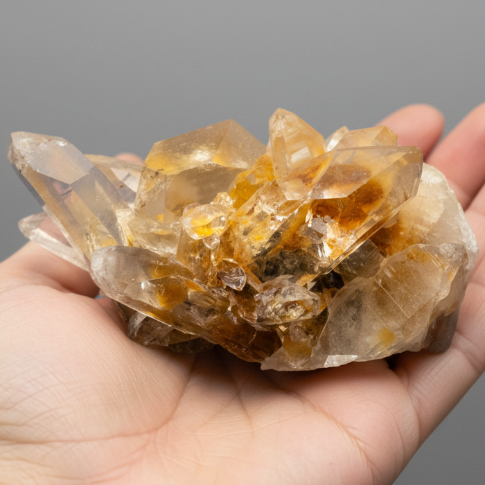 Hand holding a cluster of clear and amber-colored crystals against a gray background