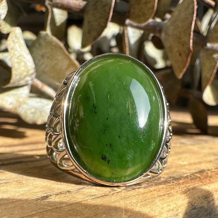 Green jade stone ring with silver band on a wooden surface
