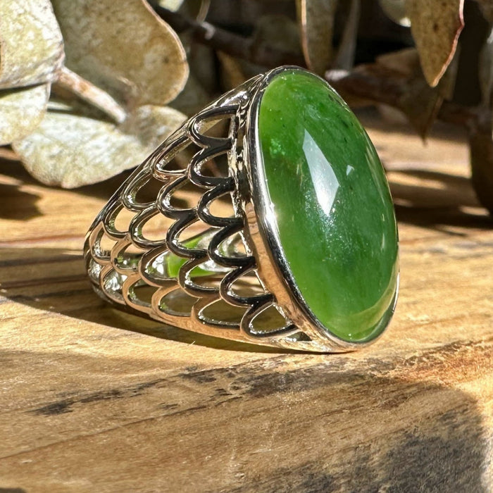 Silver ring with a green jade stone on a wooden surface with eucalyptus leaves in the background