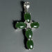 Green cross pendant with silver accents on a wooden surface