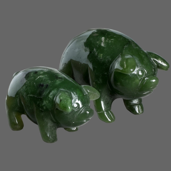 Two green jade pig figurines on a wooden surface with a stone vase in the background.