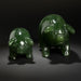 Two green pig figurines on a wooden surface with a ceramic vase in the background.