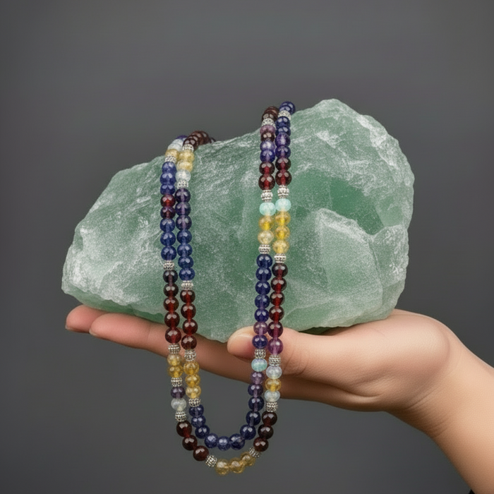beaded necklaces held against a large green fluorite crystal on a dark background