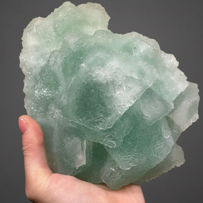 Hand holding a large green crystal against a dark background