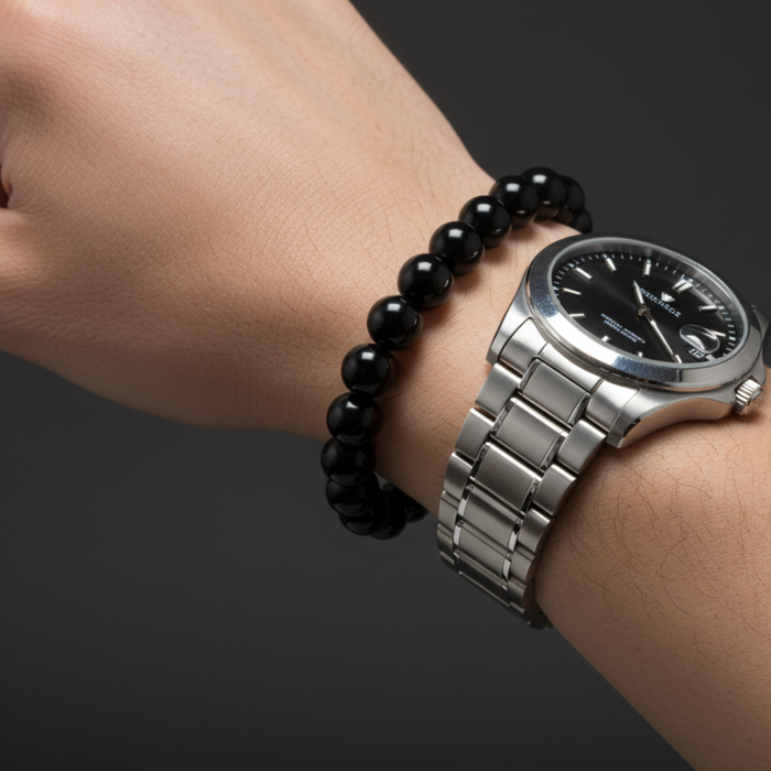 Silver watch and black onyx beaded bracelet on a wrist against a dark background
