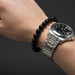 Silver watch and black onyx beaded bracelet on a wrist against a dark background