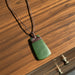 Green pendant on a brown cord with leaves in the background