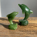 Two green jade dolphin sculptures on a wooden surface