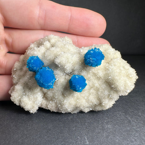 Rock with blue crystals held in a hand against a dark background