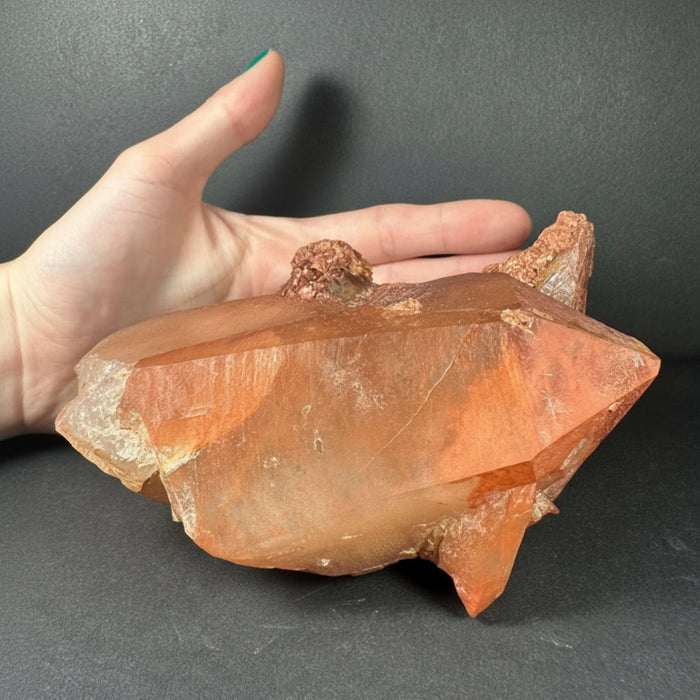 Hand holding a large orange crystal against a dark background
