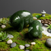 Two green jade pigs on a miniature landscape with plants and a bridge.