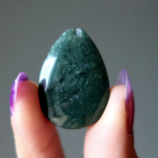 Hand holding a green Moss Agate stone against a gray background