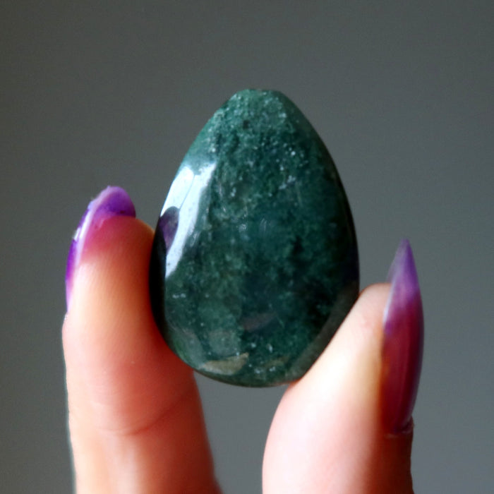 Green Moss Agate stone held between fingers with a gray background