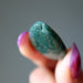 Green stone held between fingers with a blurred background