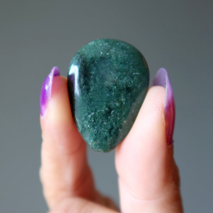 Hand holding a green Moss Agate stone against a gray background