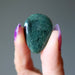 Hand holding a green Moss Agate stone against a gray background