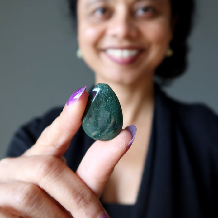 Person holding a green Moss Agate stone with a blurred background