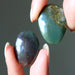 Two polished moss agate stone gemstones held between fingers against a neutral background