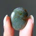 Hand holding a greenish-blue moss agate stone against a dark background