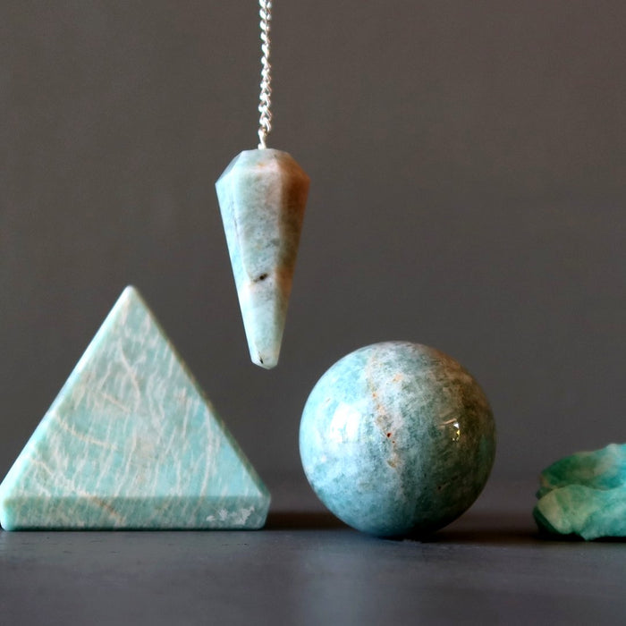 Set of amazonite crystal shapes including a pyramid, sphere, and pendulum on a dark background