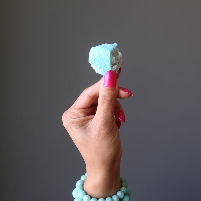 Hand holding a blue amazonite crystal against a gray background