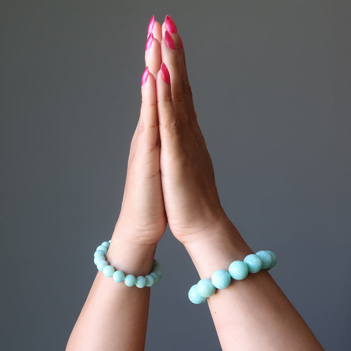 Two hands with amazonite beaded bracelets on a gray background