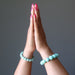 Two hands with amazonite beaded bracelets on a gray background