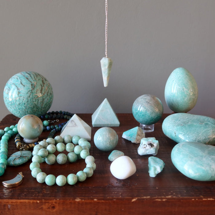 Collection of amazonite stones, beads, and a pendulum on a wooden surface with a gray background.