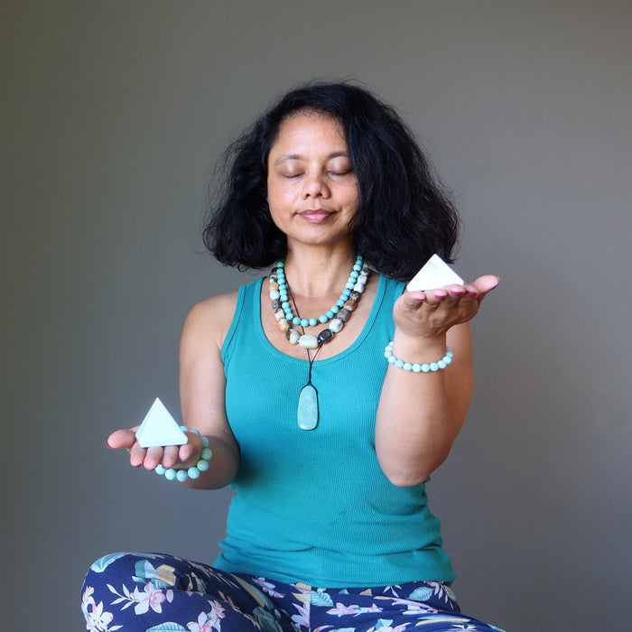 Woman in teal tank top holding two amazonite pyramids against a gray background