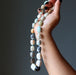 Hand holding a necklace with multicolored Amazonite beads against a dark background