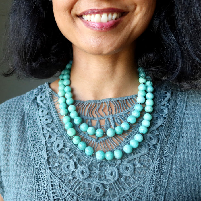 Woman wearing an Amazonite beaded necklace with a gray lace top against a neutral background