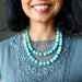 Woman wearing an Amazonite beaded necklace with a gray lace top against a neutral background