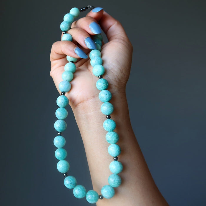 Hand holding an Amazonite beaded necklace against a dark background